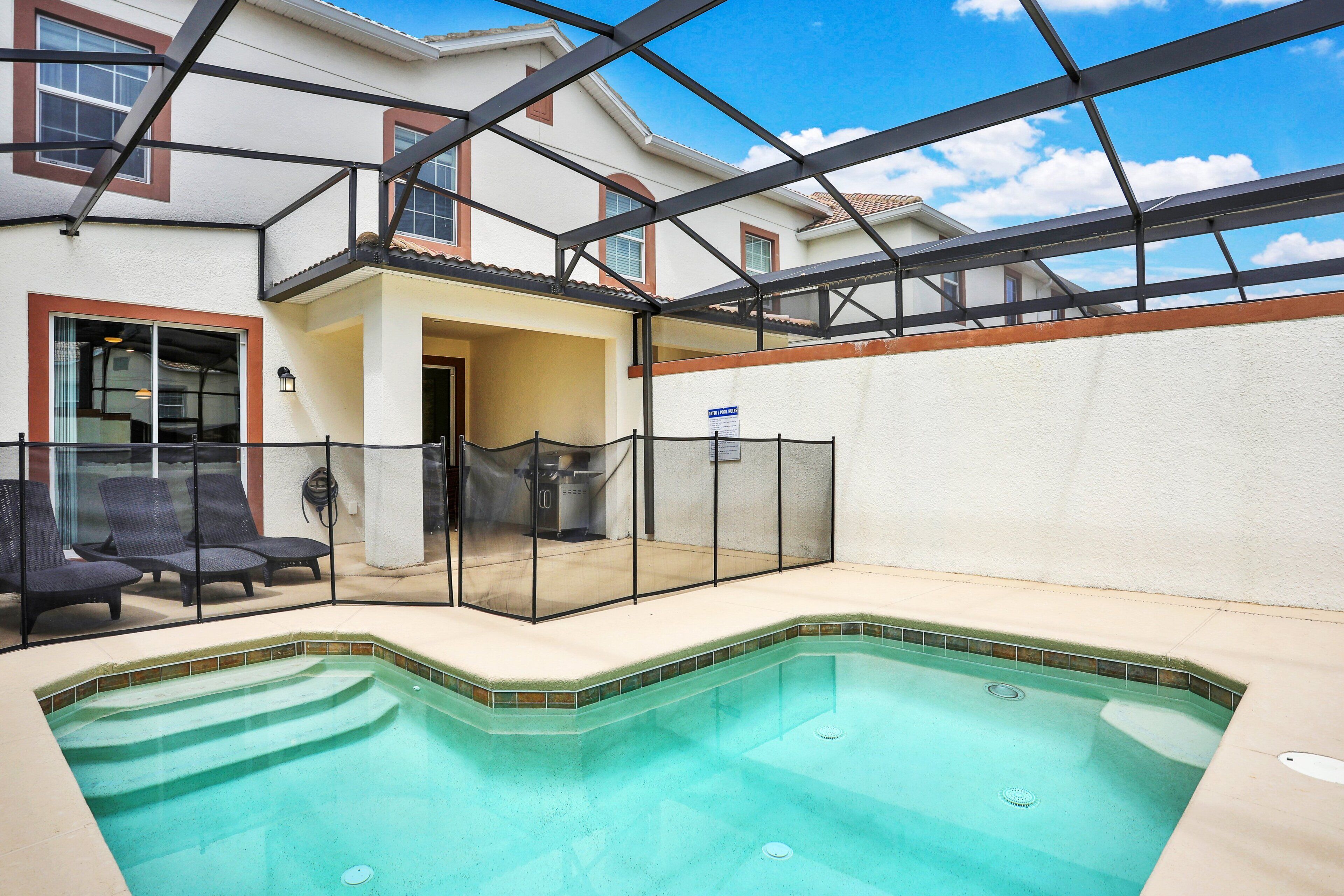 A swimming pool with a glass enclosure, a covered patio area, and a view of a residential building.