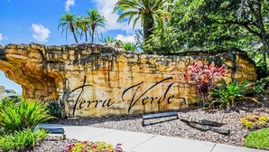 A stone wall with 'Terra Verde' written on it, surrounded by tropical plants and a paved walkway. - Beautiful & Spacious Resort Home in the Heart of Central FL (Kissimmee)