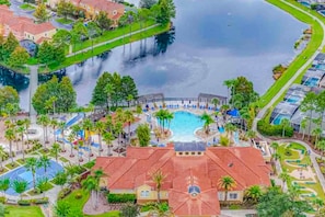 Vista aérea de um resort com piscina central, caminhos ao redor e um corpo d'água.