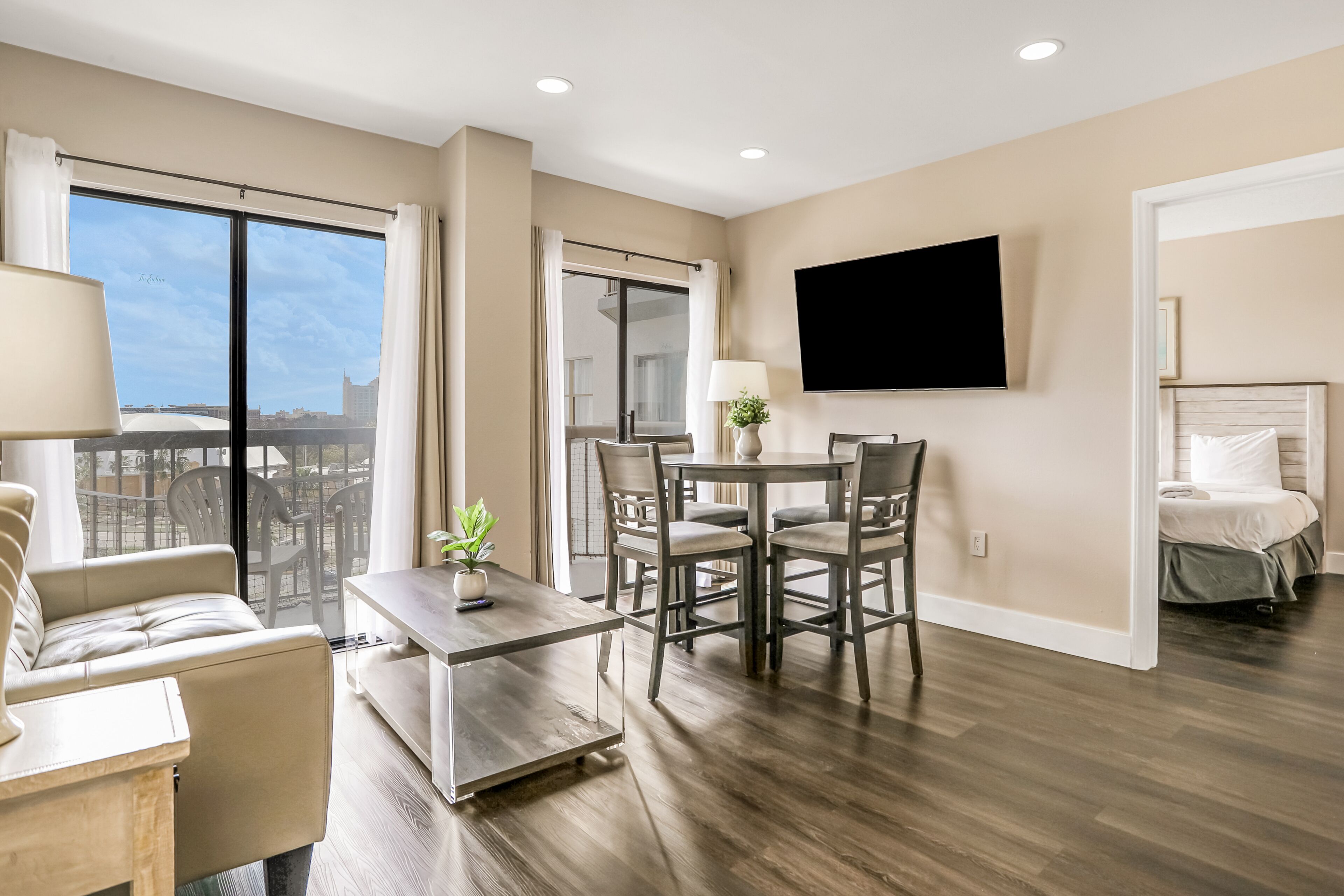 Une chambre d’hôtel moderne dotée d’un coin repas, d’un canapé, d’une télévision à écran plat et d’un balcon offrant une vue sur la ville.
