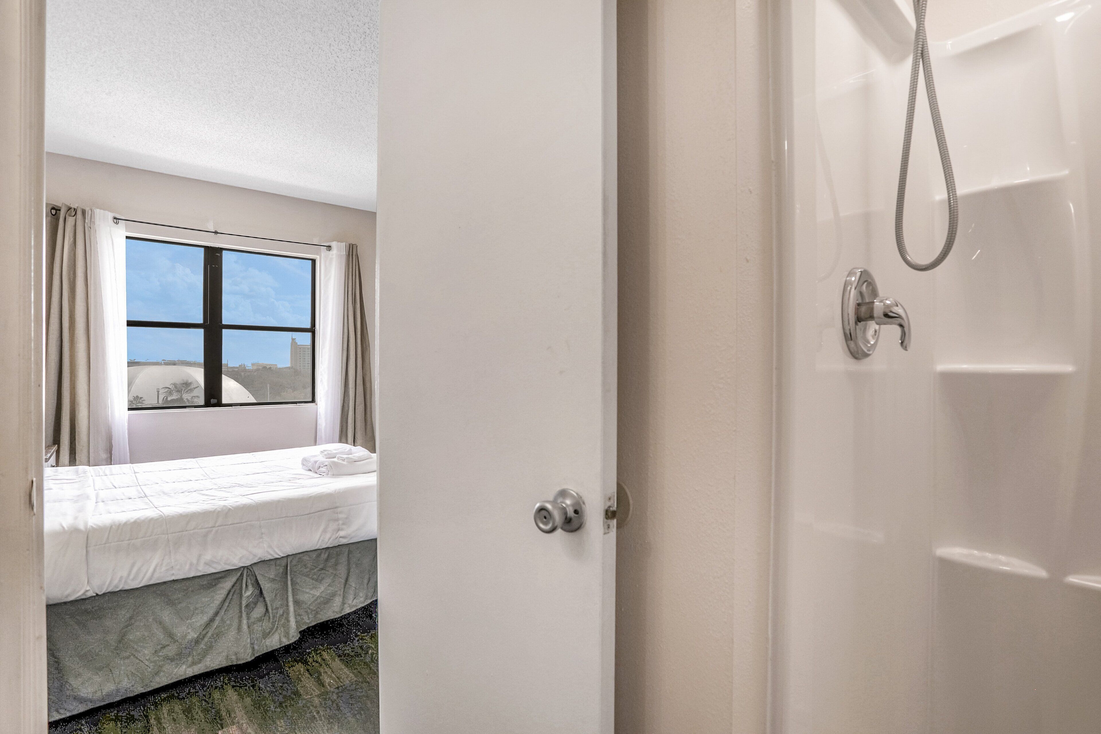 Habitación de hotel con cama, ventana con cortinas y zona de ducha.
