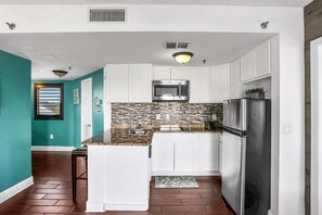 A kitchen with white cabinets, a stainless steel refrigerator, a microwave, and a tiled backsplash. - Orlando Escape - Carrier Dr (Orlando)