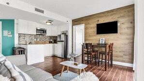 A modern kitchen with white cabinets, a built-in microwave, and a refrigerator. There is a dining area with a wooden table and chairs.