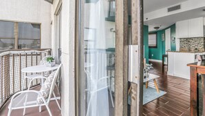 A balcony with a table and chairs, a kitchen area with teal walls, and a wooden floor.