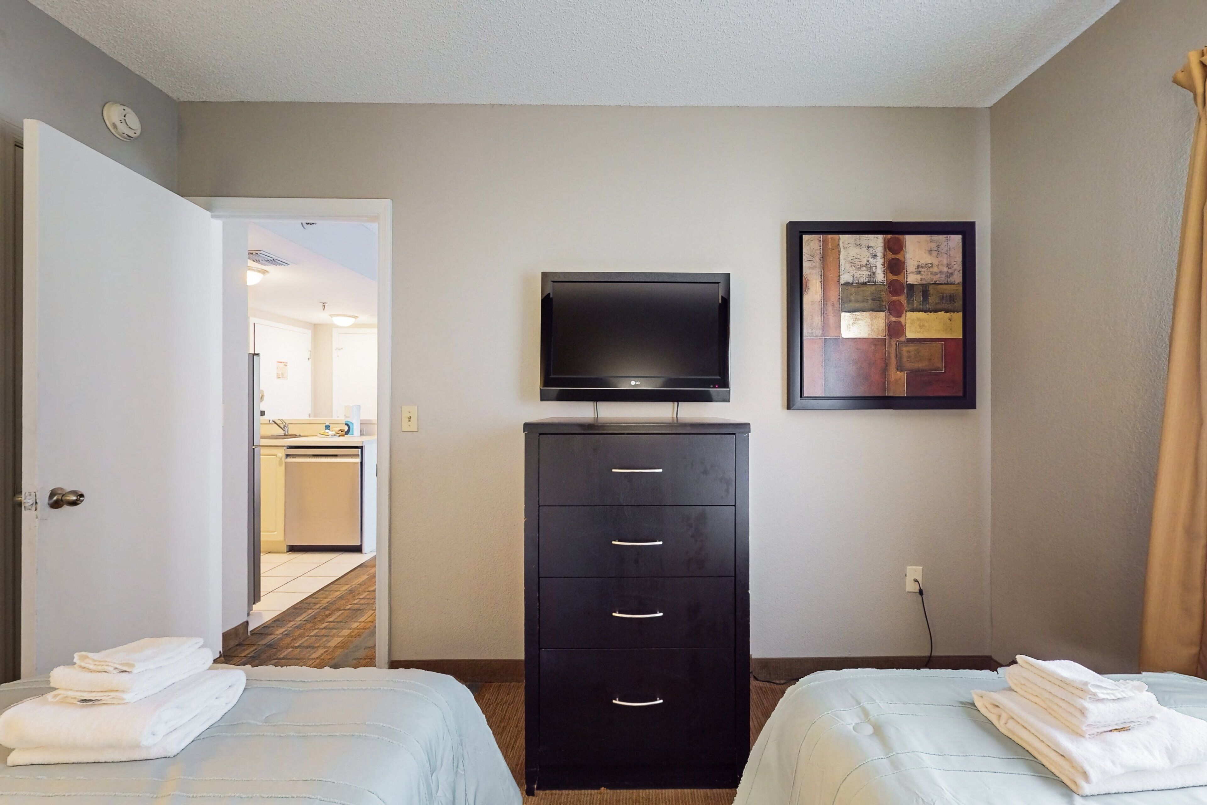 A hotel room with two beds, a TV, a cabinet, and a painting on the wall.