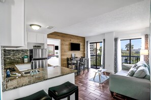 A modern kitchen with a granite countertop, stainless steel appliances, and a dining area with a table and chairs. - Orlando Escape - Carrier Dr (Orlando)