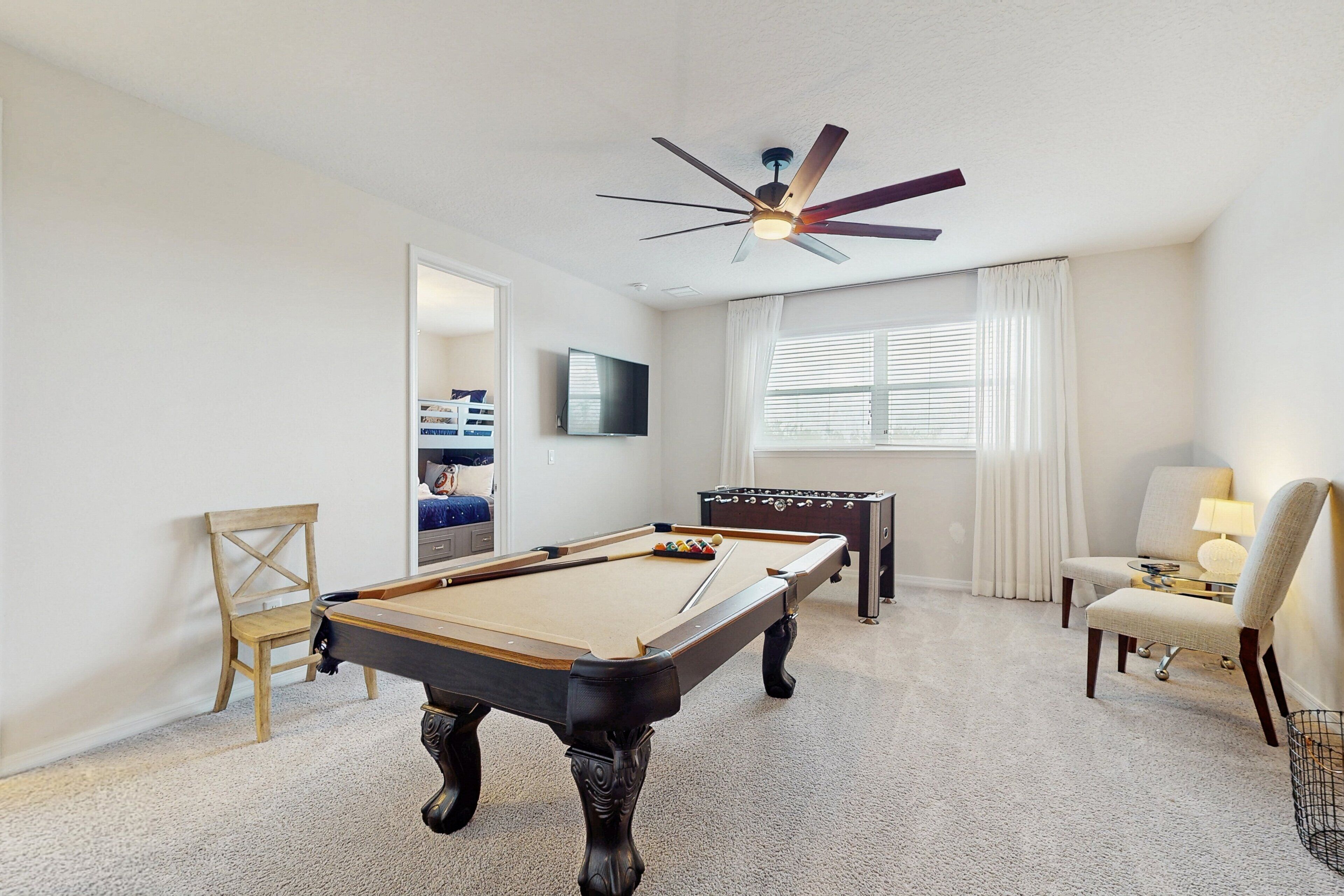 A pool table, a foosball table, a ceiling fan, a TV, and a window with curtains.