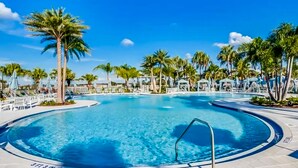 A large, clear swimming pool surrounded by palm trees and lounge chairs, with a clear blue sky above. - Solara Joy Disney-themed Retreat in Kissimmee With Stellar Resort Amenities (Kissimmee)