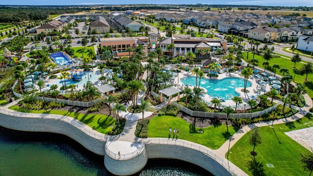 A resort with a central swimming pool, a bridge over water, and a well-maintained lawn. - Solara Joy Disney-themed Retreat in Kissimmee With Stellar Resort Amenities (Kissimmee)