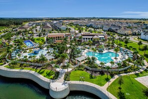 A resort with a central swimming pool, a bridge over water, and a well-maintained lawn. - Solara Joy Disney-themed Retreat in Kissimmee With Stellar Resort Amenities (Kissimmee)