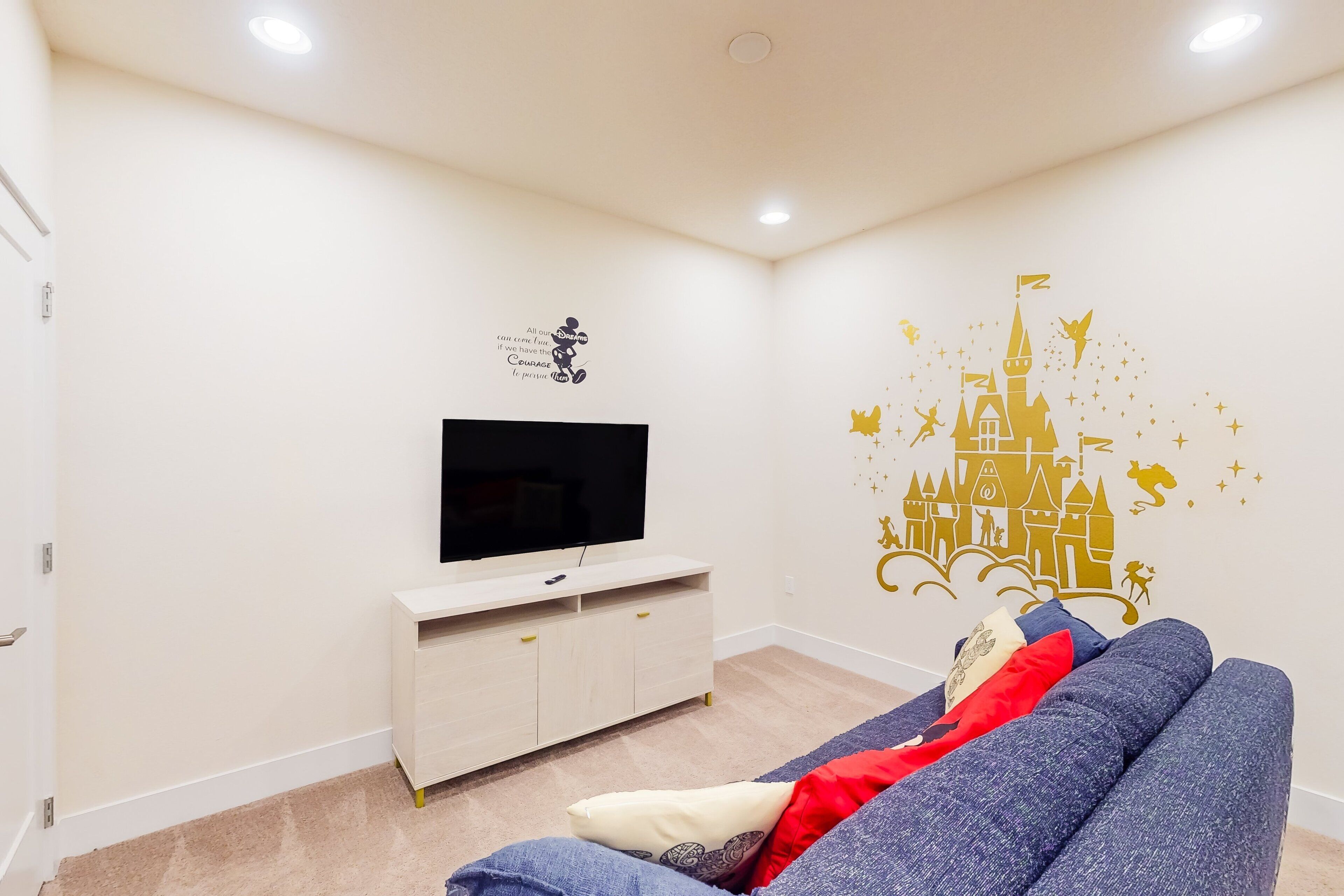 A room with a TV on a stand, a blue sofa, and a wall decal of a castle.
