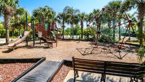Ein Spielplatz mit Rutschen und Klettergerüsten, umgeben von Palmen.