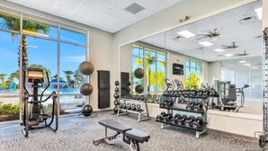 Et fitnesscenter med træningsudstyr, store vinduer og udsigt til palmer.