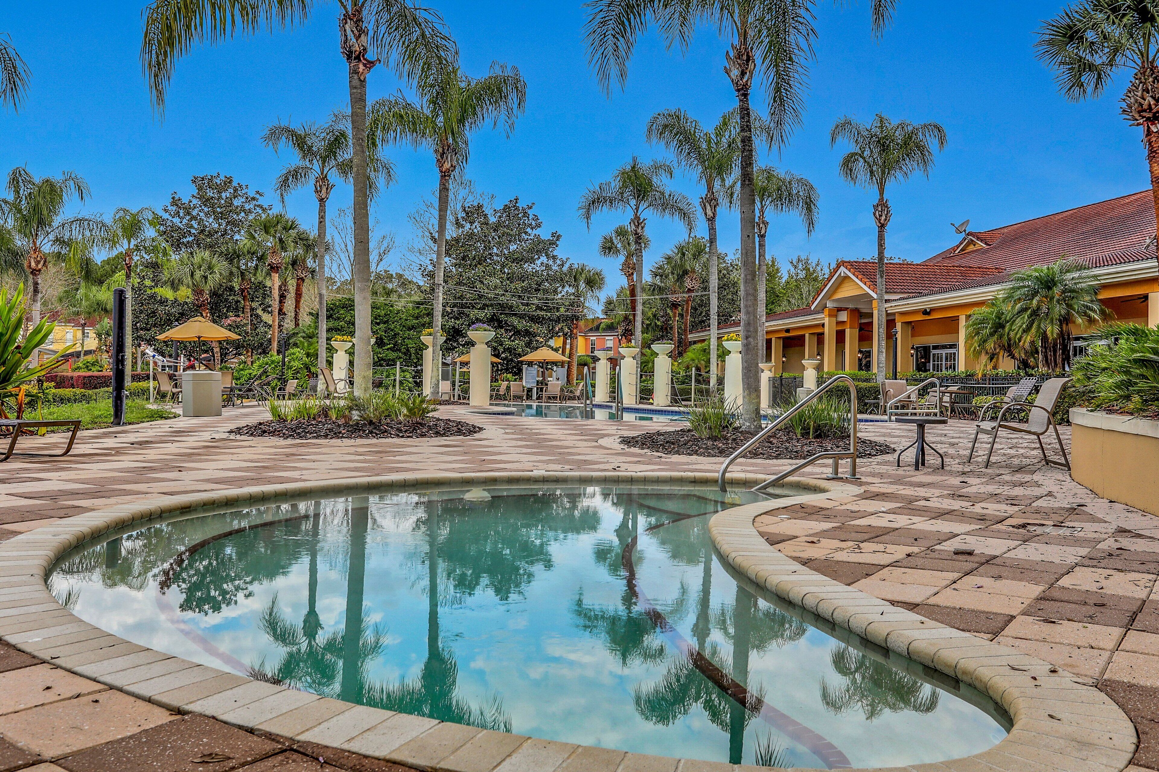 A pool area with palm trees, a covered seating area, and a building with a tiled roof.