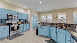 A kitchen with blue cabinets, a stainless steel oven, a microwave, granite countertops, and a window with blinds. - Beautiful Home With Private Pool and Space for the Whole Family (Kissimmee)