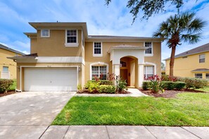 A two-story residential building with a garage, a well-maintained lawn, and a palm tree. - Beautiful Home With Private Pool and Space for the Whole Family (Kissimmee)