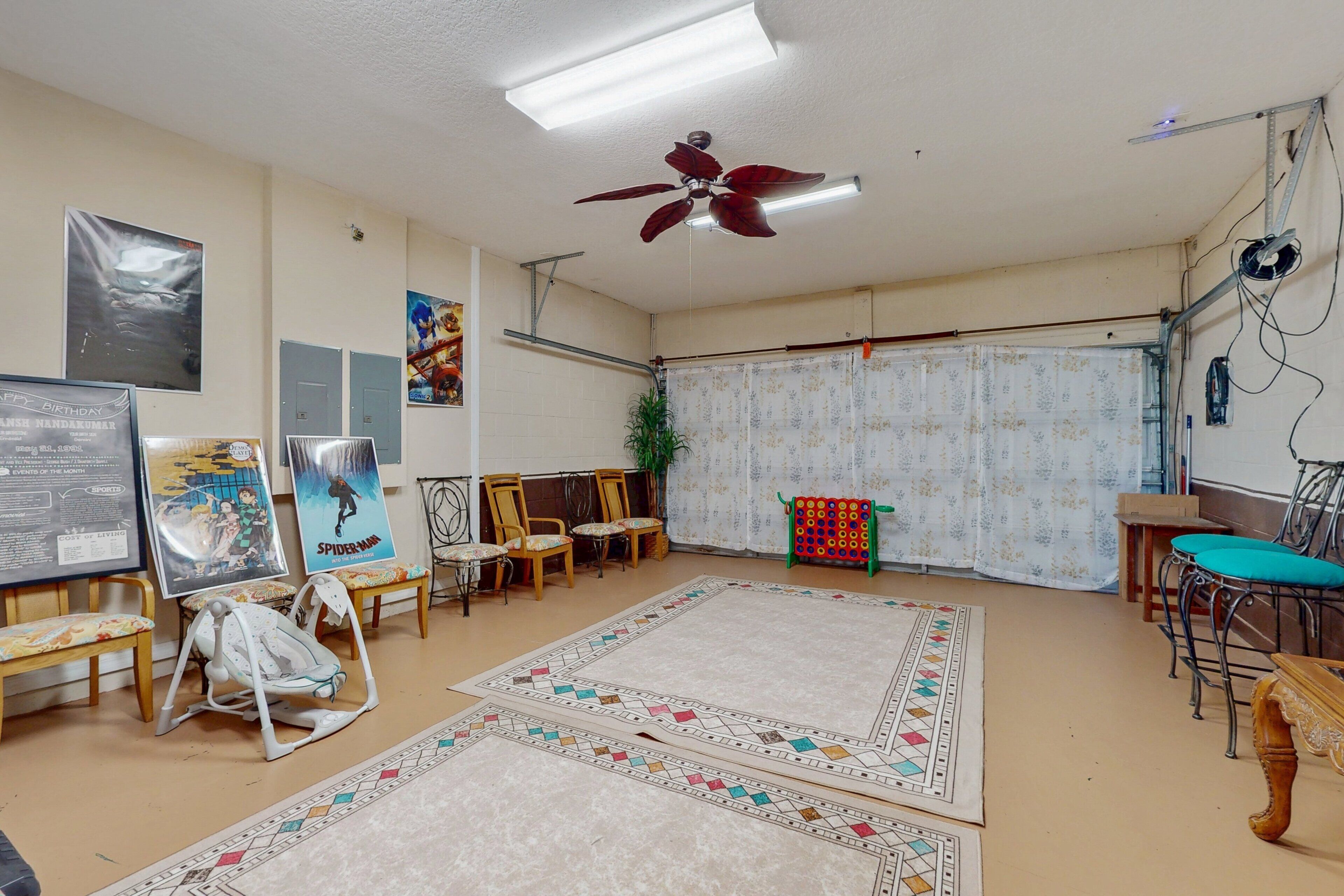 Una habitación con ventilador de techo, alfombra grande, varias sillas, una bicicleta y carteles en las paredes.