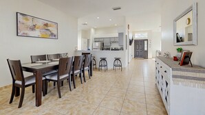 Una cuina moderna amb armaris foscos, una illa central i una zona de menjador amb taula gran i cadires.