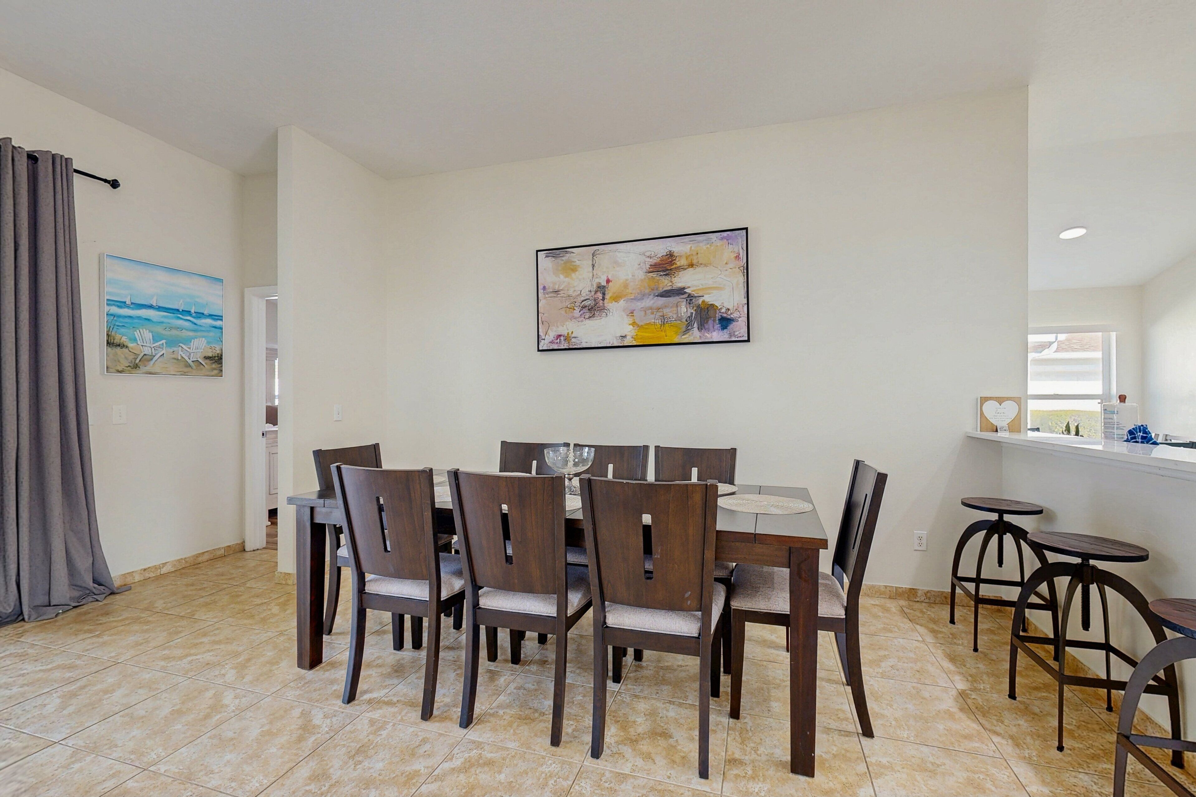 A dining area with a table and chairs, a painting on the wall, and a window with a view.