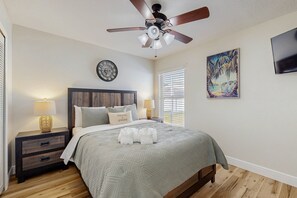Une chambre à coucher comprenant un lit, des tables de chevet, un ventilateur de plafond, une horloge, un tableau et un téléviseur.