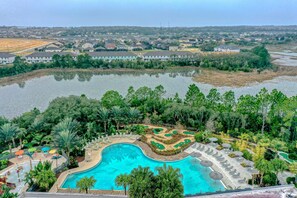 A swimming pool surrounded by lush greenery, with a view of a residential area in the background. - No Worries Retreat Disney-themed Townhouse in Davenport With Resort Amenities (Davenport)