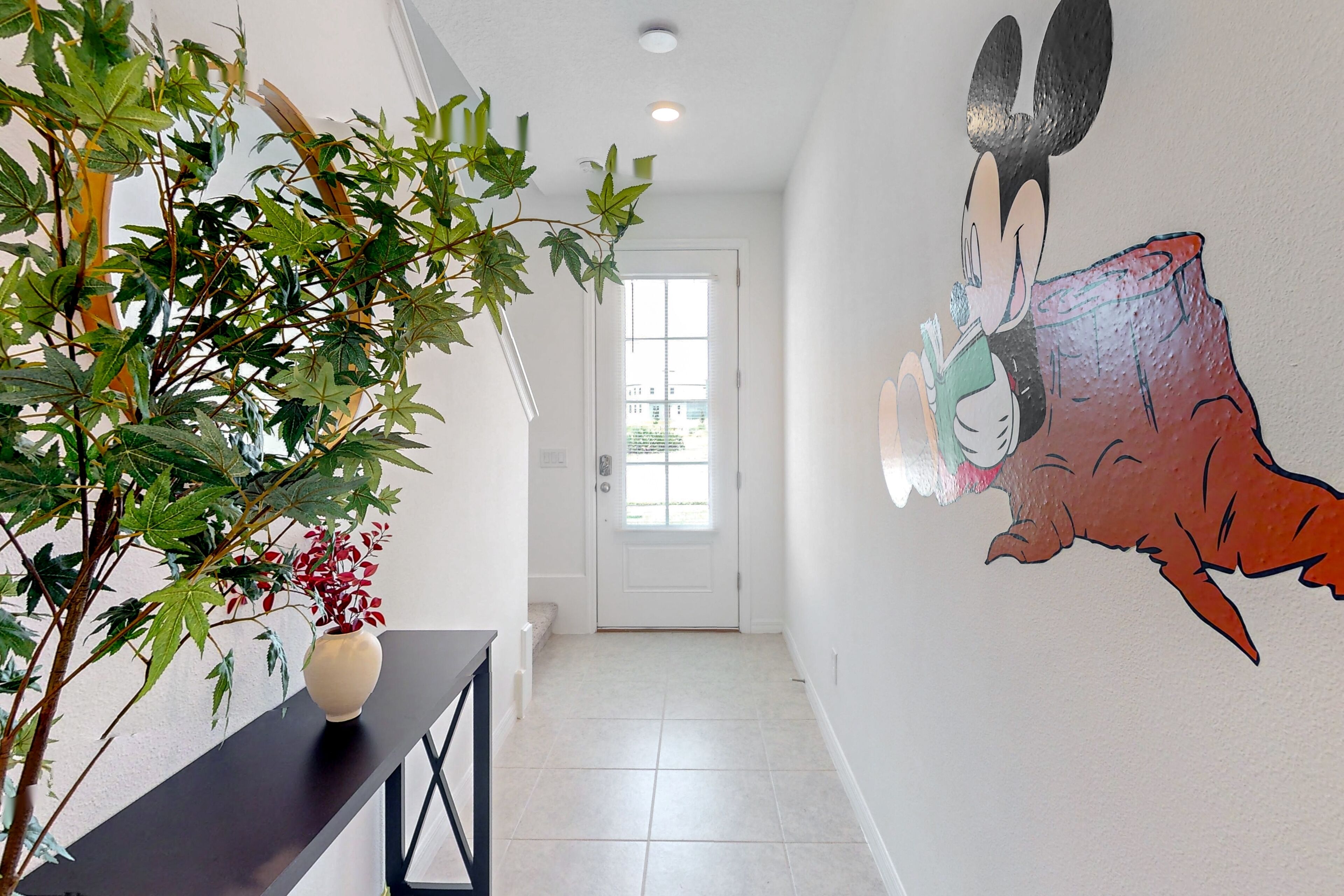 A hallway with a potted plant, a white door, and a wall mural of a cartoon character.