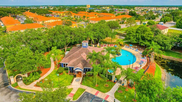 An aerial view of a resort with a swimming pool, lush greenery, and a mix of residential and commercial buildings. - Spacious Family Friendly Home With Resort Style Shared Pool (Kissimmee)