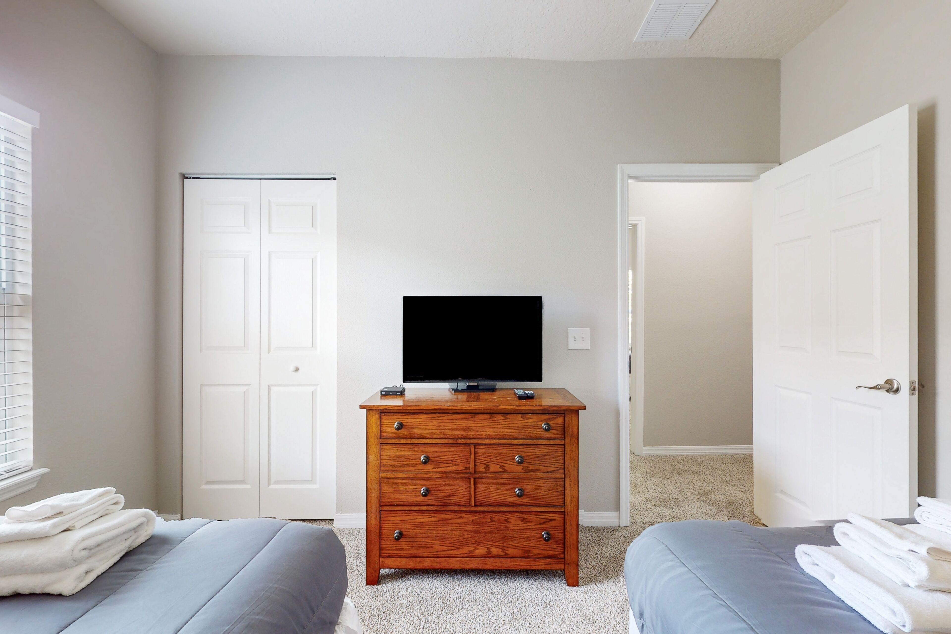 A bedroom with a wooden dresser, a television, two beds, and white doors.