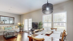A spacious living room with a wooden dining table, comfortable seating, a large mirror, and a television. - Spacious Family Friendly Home With Resort Style Shared Pool (Kissimmee)