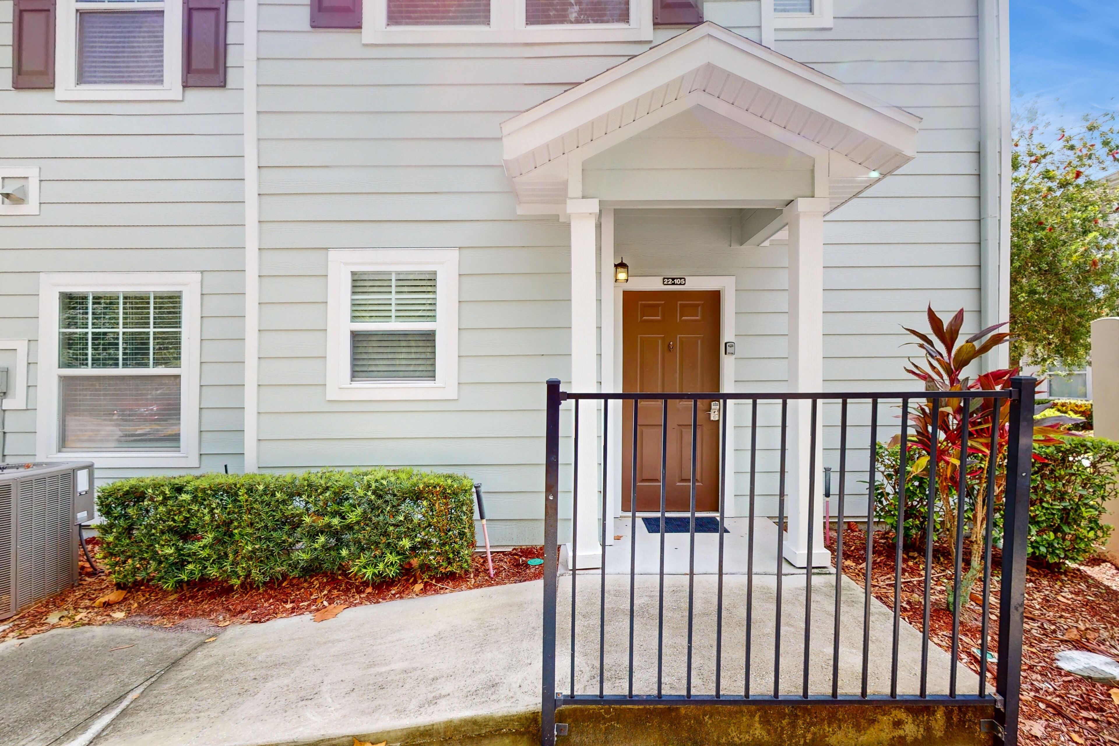 A two-story building with a front entrance, a mailbox, and a small garden area with a metal gate.