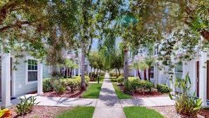 A pathway flanked by white buildings with green lawns and trees. - Spacious Family Friendly Home With Resort Style Shared Pool (Kissimmee)