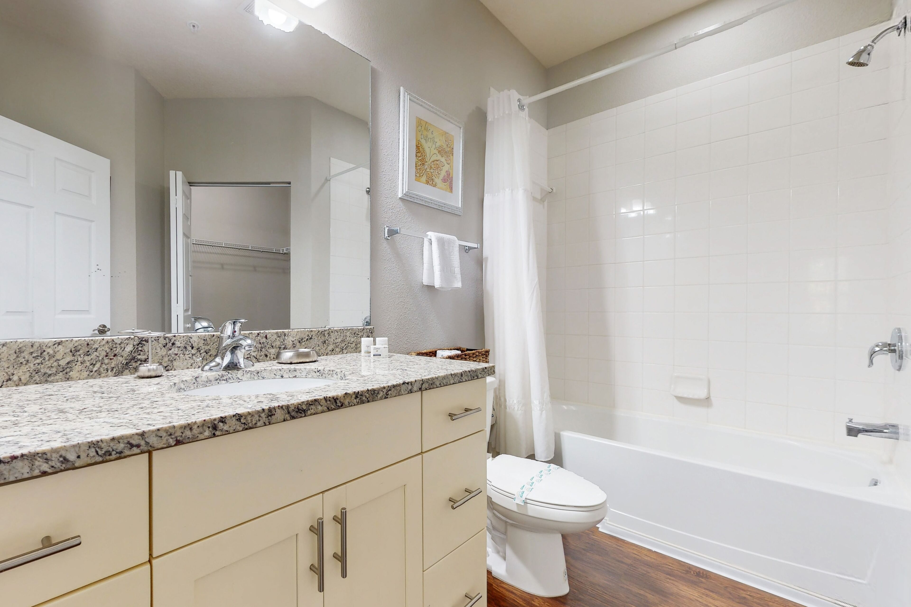 Un baño con inodoro blanco, bañera, ducha y tocador con encimera de granito.