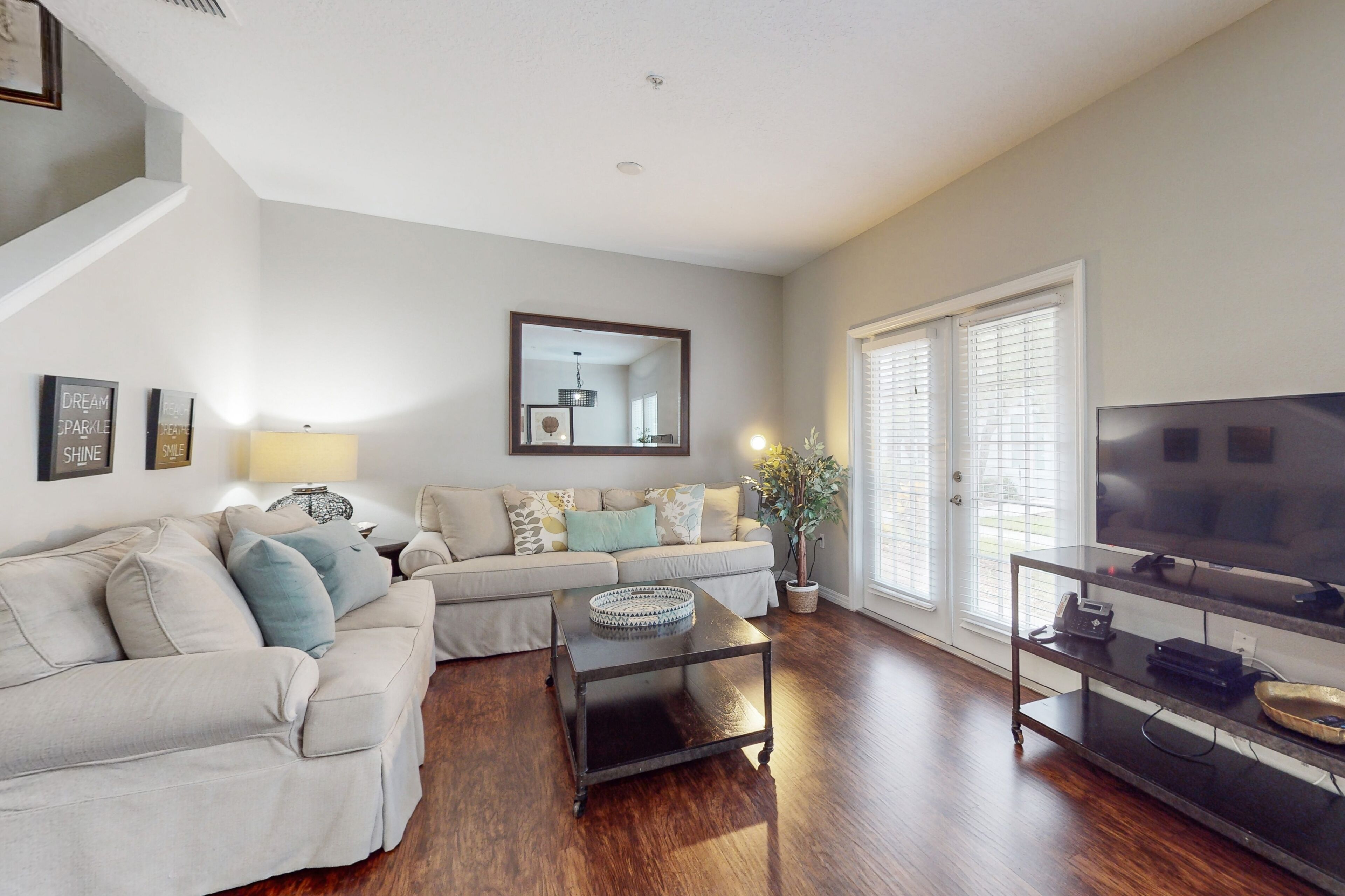 A living room with a sectional sofa, a coffee table, a TV on a stand, and a large window with blinds.