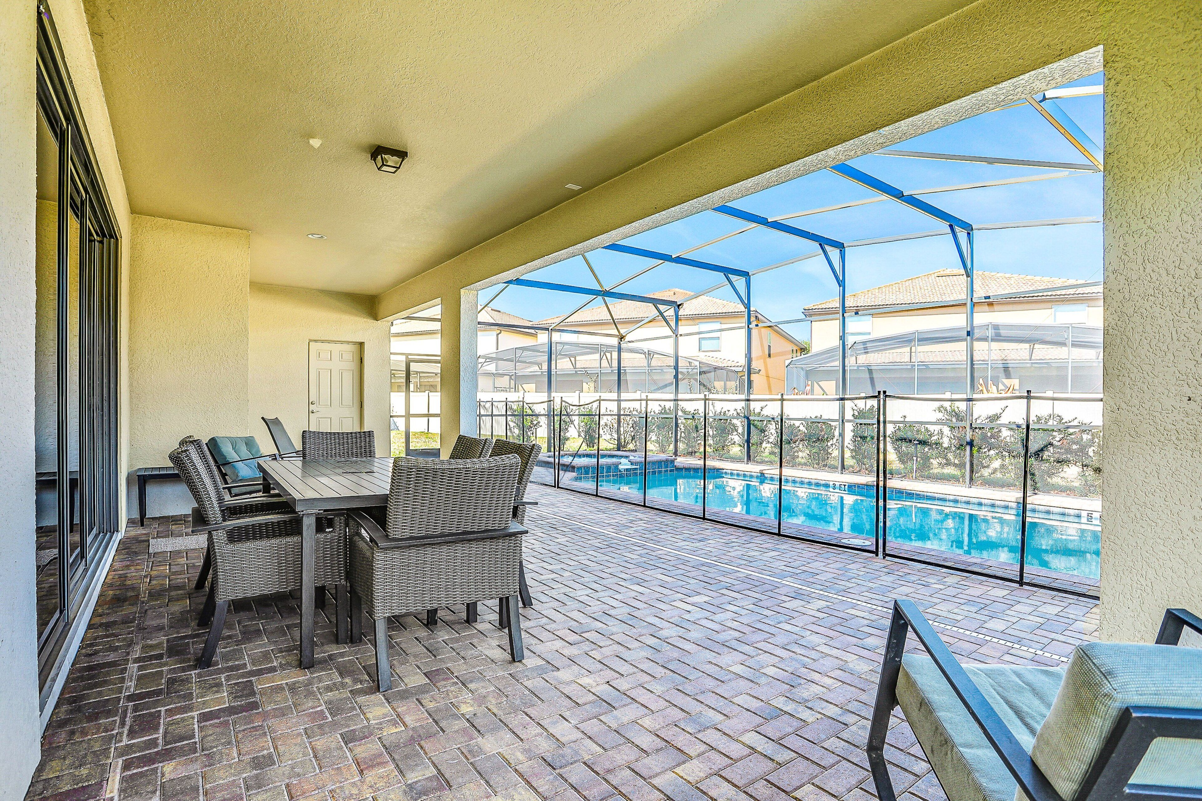 A covered patio with a pool, wicker furniture, and a brick floor.