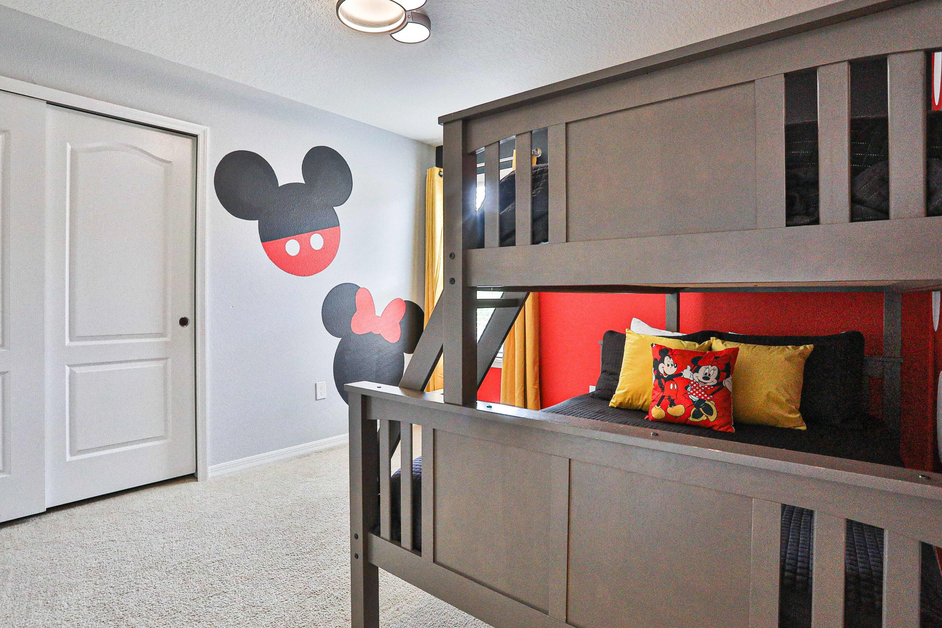 A bunk bed with Mickey Mouse wall decals, a door, and a red cushion.