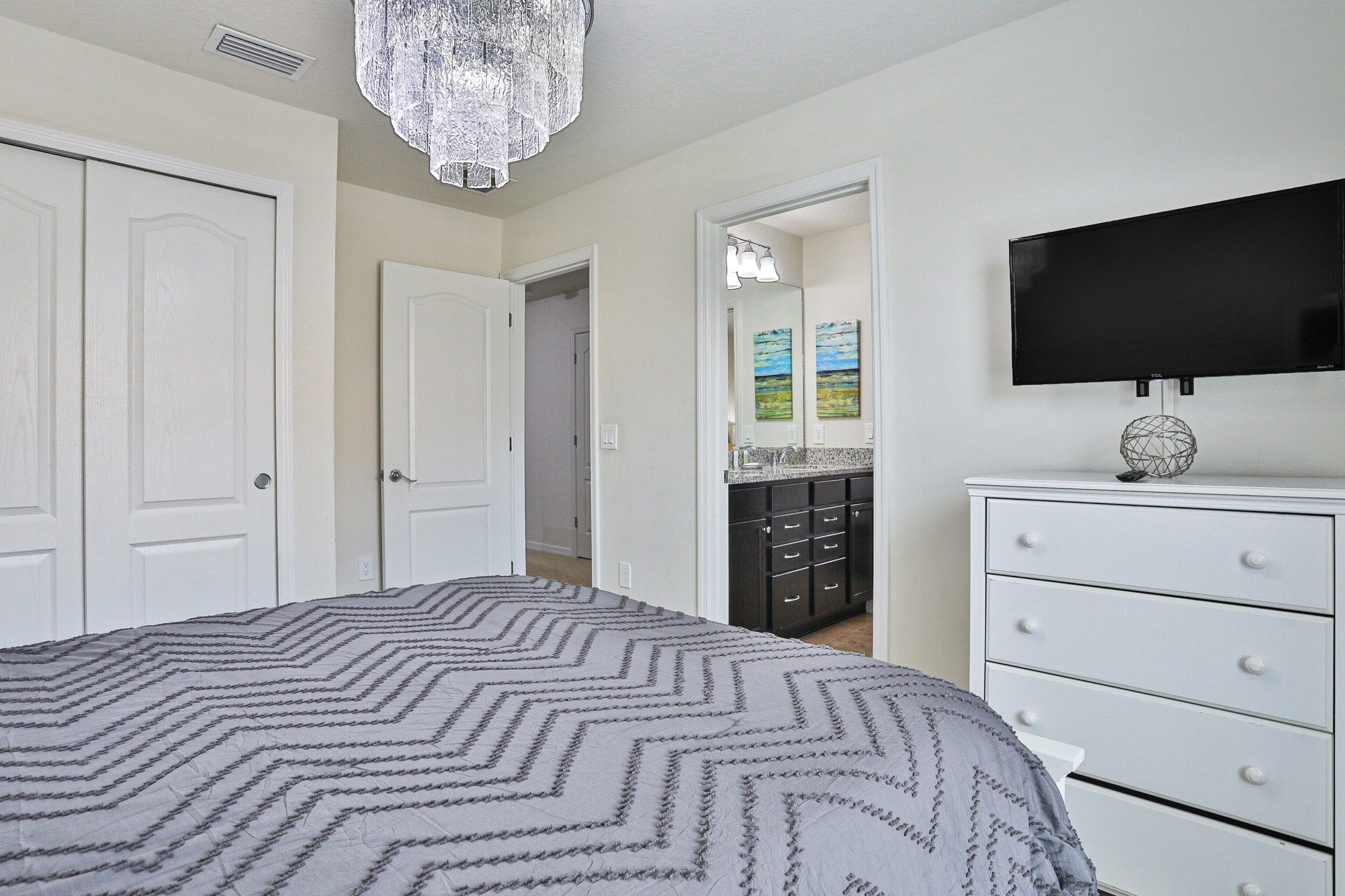 A bedroom with a bed, a dresser, a television, and a chandelier.