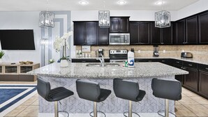 A modern kitchen with dark cabinets, a granite countertop, stainless steel appliances, and pendant lighting. - Gorgeous Home With Private Pool With Spa, Pool Table & gas Grill (Kissimmee)