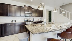 A modern kitchen with dark cabinets, a granite island, stainless steel appliances, and pendant lighting. - Beautiful Home With Private Pool and Space for the Whole Family (Davenport)
