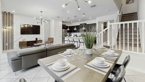 A modern dining area with a wooden table set for six, a grey sofa, and a kitchen in the background. - Beautiful Home With Private Pool and Space for the Whole Family (Davenport)