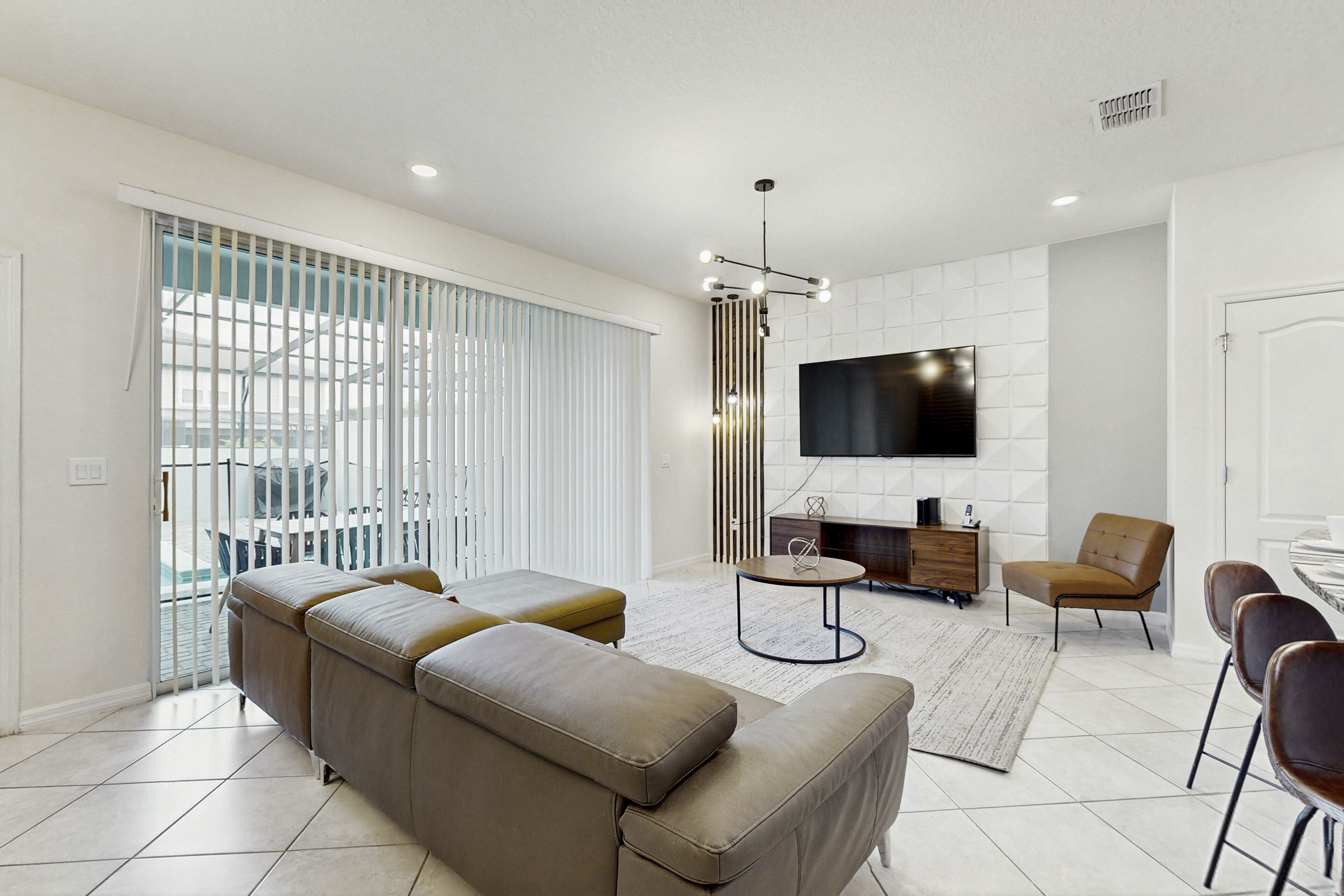 A modern living room with a sectional sofa, a TV mounted on the wall, and a dining area with chairs.