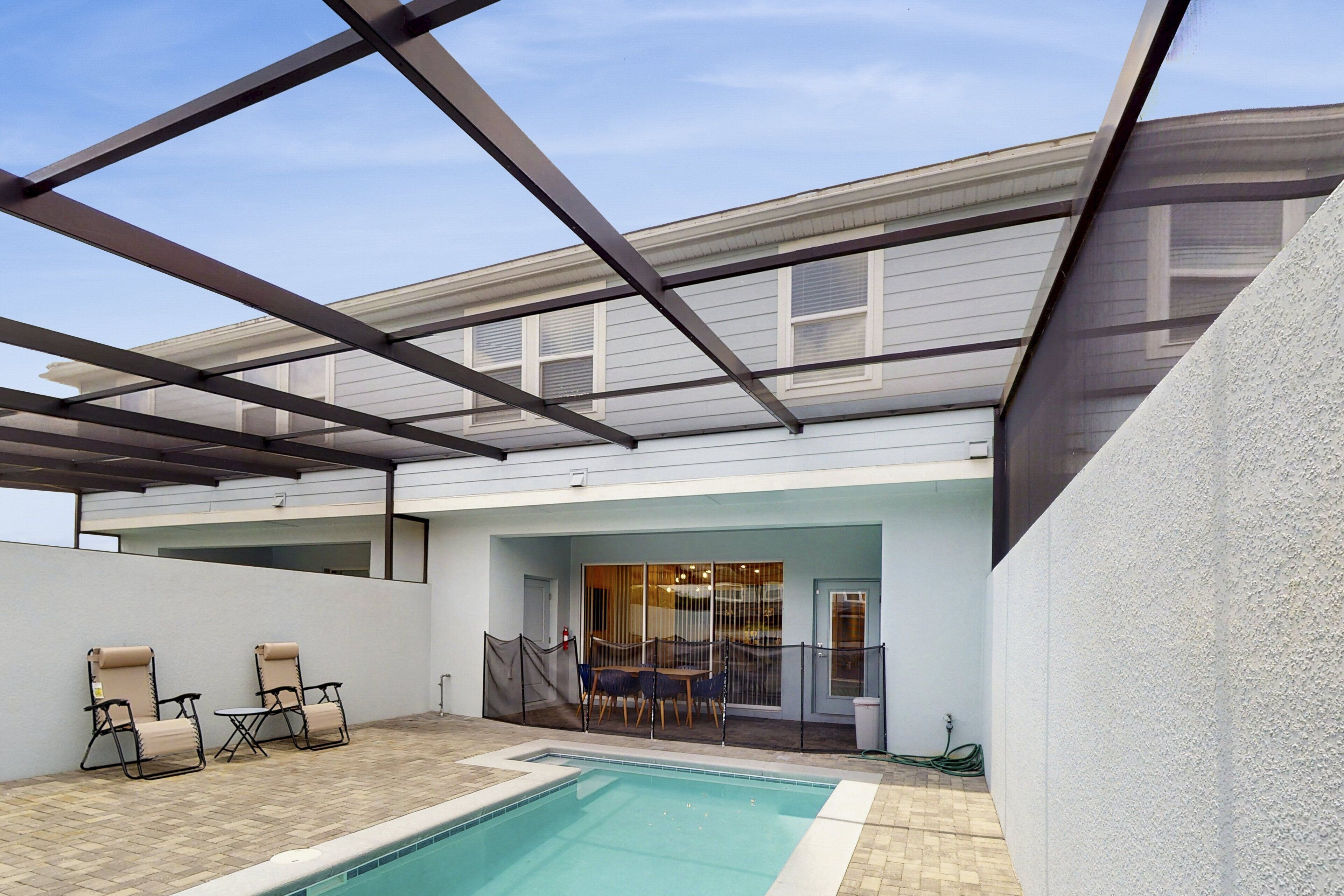 A modern outdoor pool area with a covered patio, two lounge chairs, and a table.