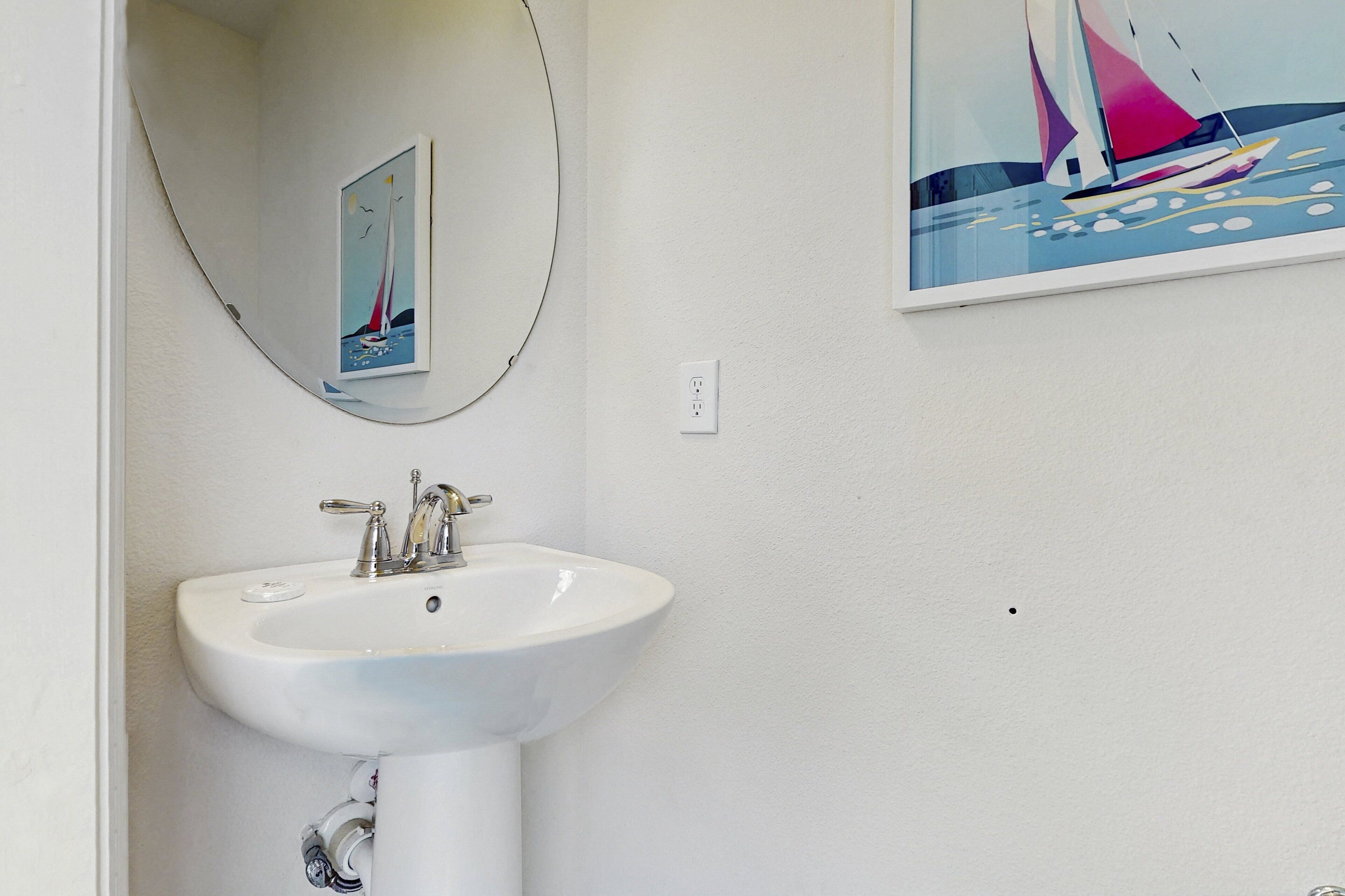 Un bagno con un lavandino bianco, uno specchio e un quadro raffigurante una barca a vela appeso al muro.