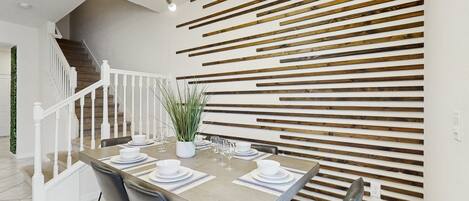 A dining area with a wooden table set for four, white chairs, a potted plant, and a staircase with white railings.