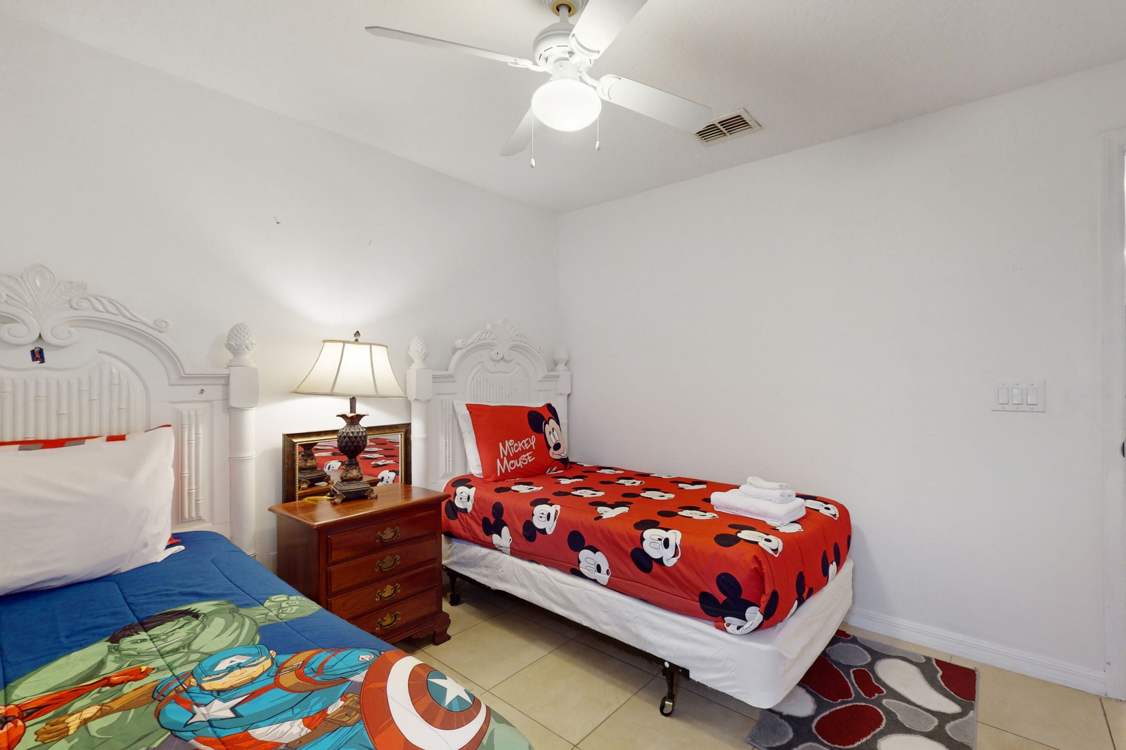 A bedroom with two beds, a ceiling fan, a lamp, and a dresser.