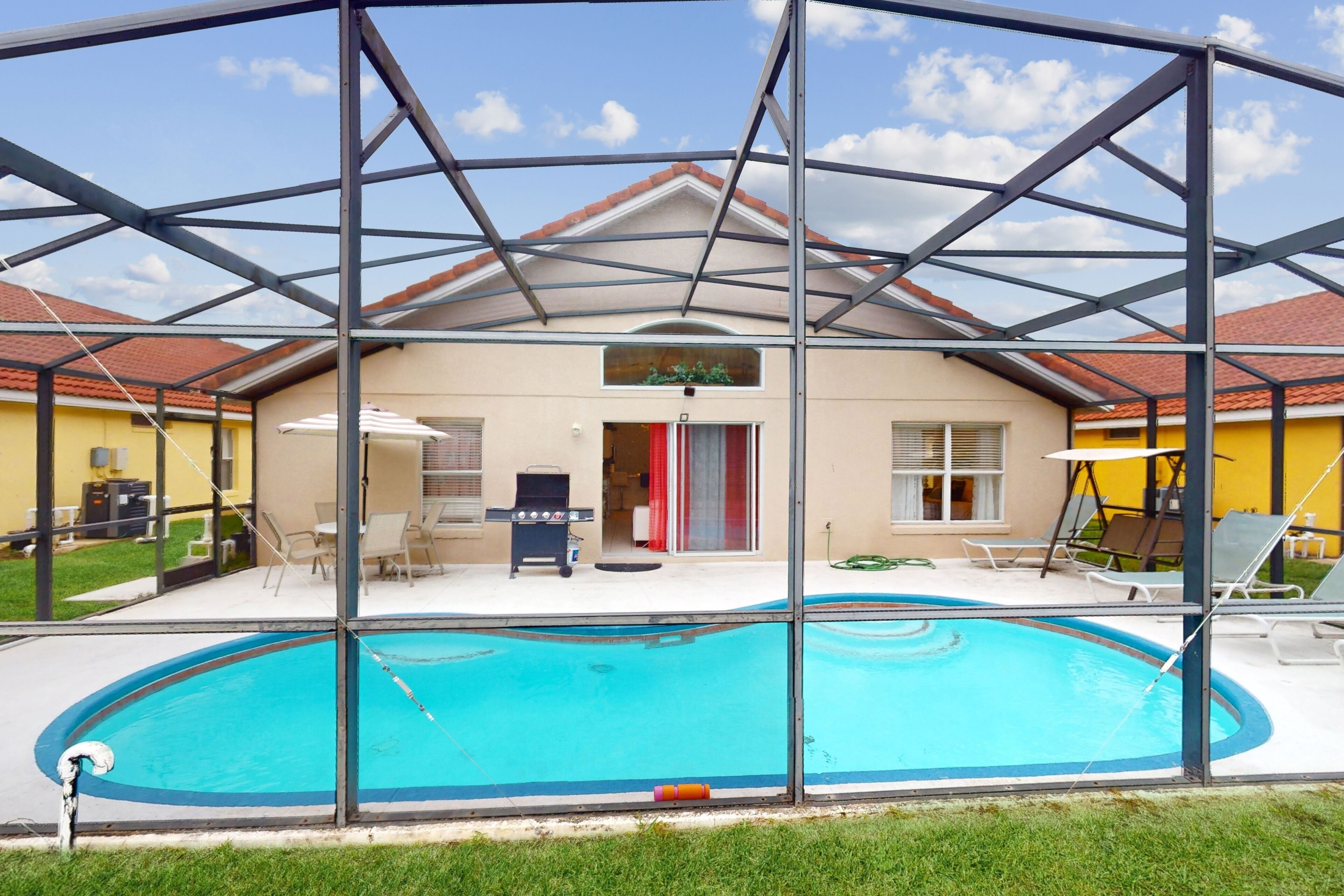 Piscina coberta com estrutura de telhado, área de churrasco e um edifício com fachada amarela.