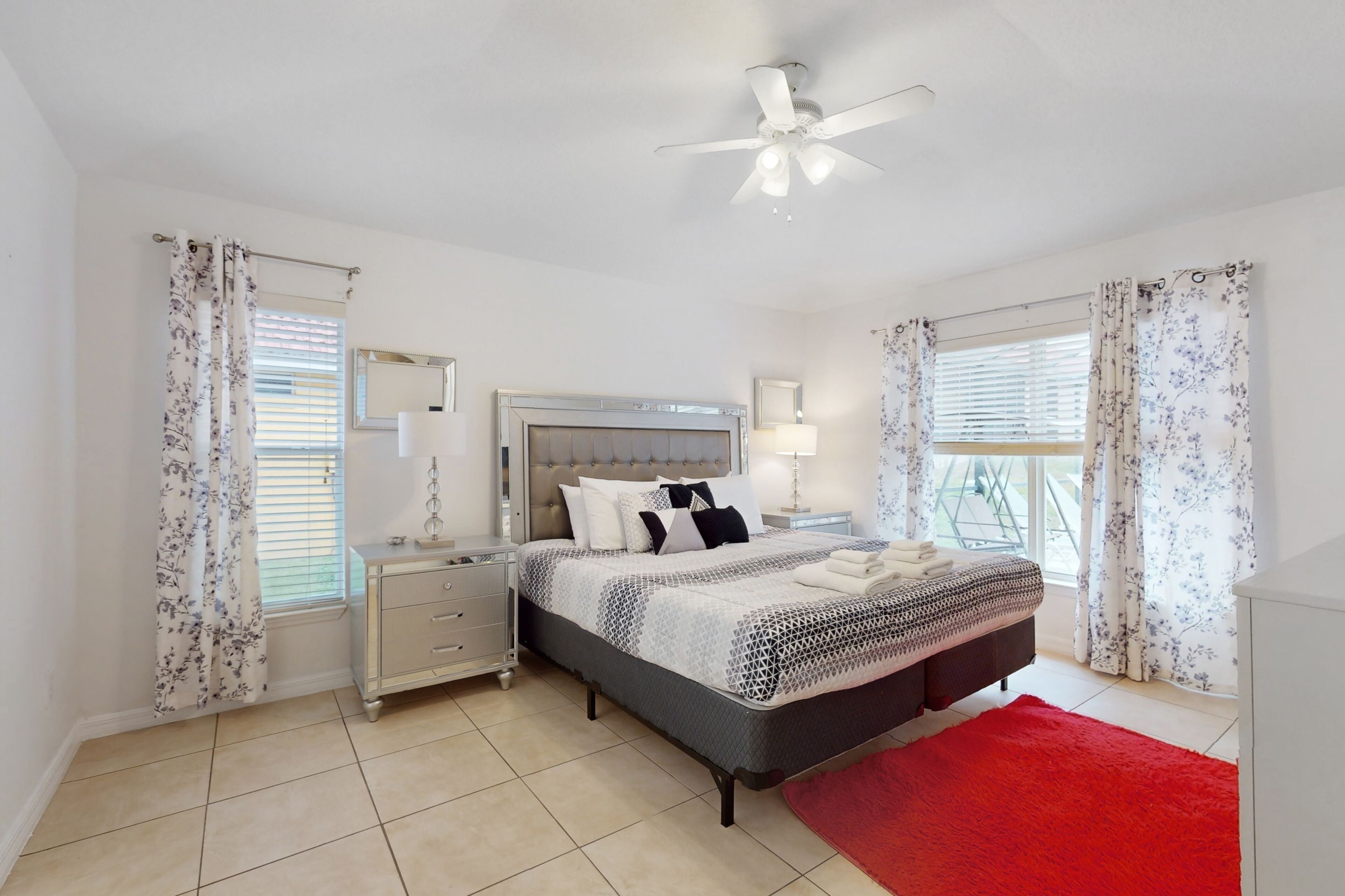 A bedroom with a bed, nightstands, a ceiling fan, and a red rug.