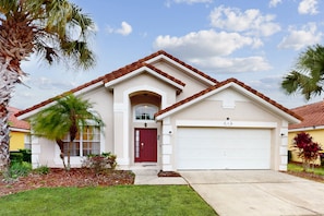 A single-story house with a red door, a garage, and a small front yard with palm trees. - Single-level Home With Private Pool, Game Room, and W/D - Near Golf/disney (Davenport)