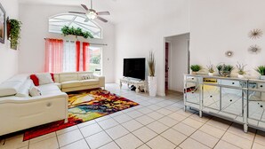 Una sala de estar con sofá, televisor, espejo decorativo, ventilador de techo y plantas en macetas.