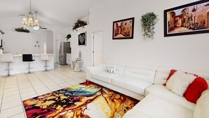 Una sala de estar moderna con un sofá blanco, una alfombra colorida y una zona de cocina con taburetes blancos.
