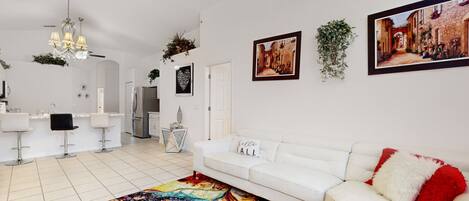 A modern living room with a white sofa, a colorful rug, and a kitchen area with white bar stools.